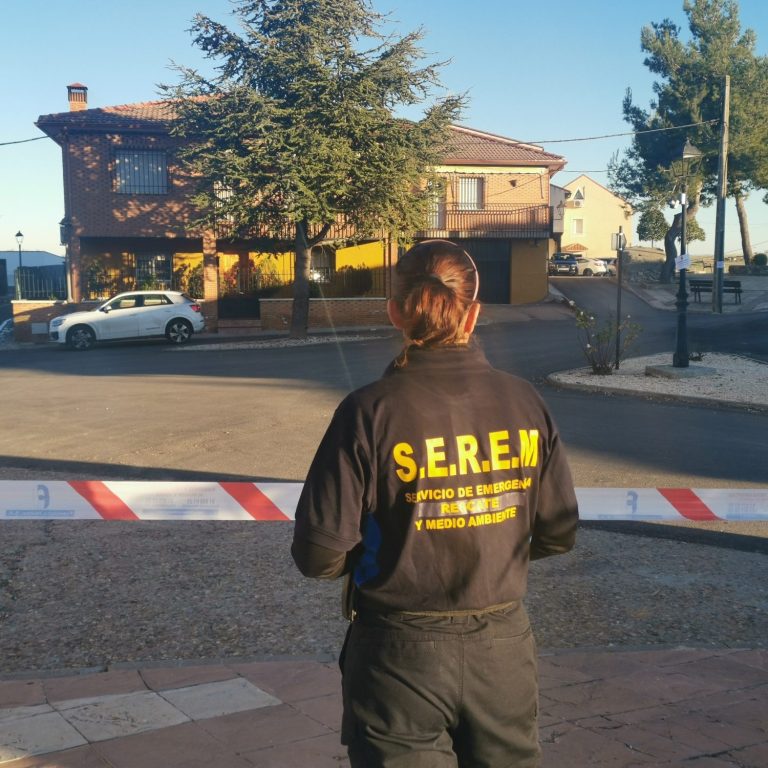 Persona de espaldas con chaqueta de la S.E.R.E.M. frente a una casa y un coche aparcado.