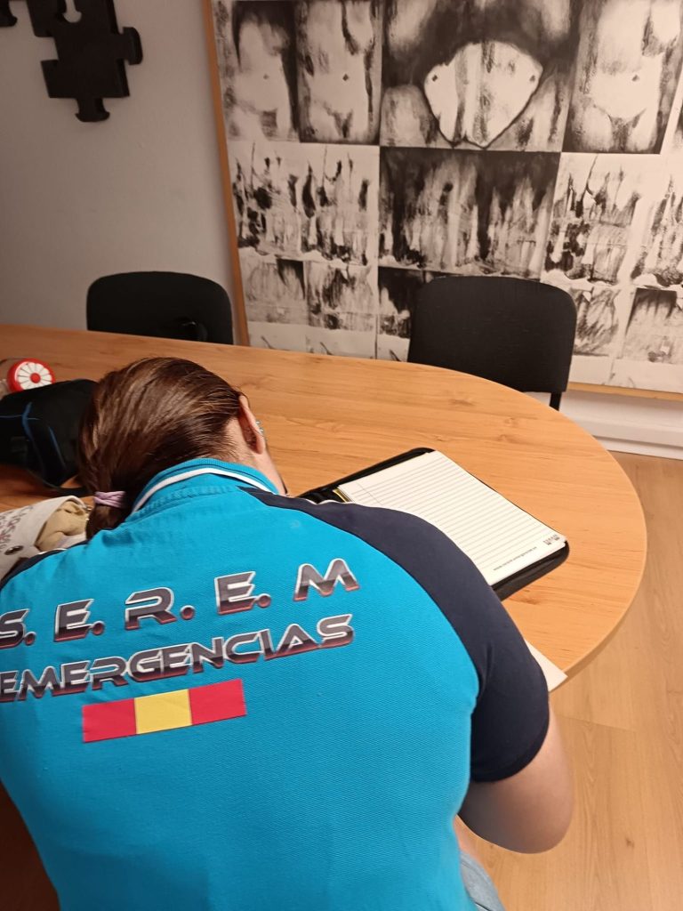 Persona sentada en una mesa con un cuaderno, vistiendo una camiseta de emergencias.